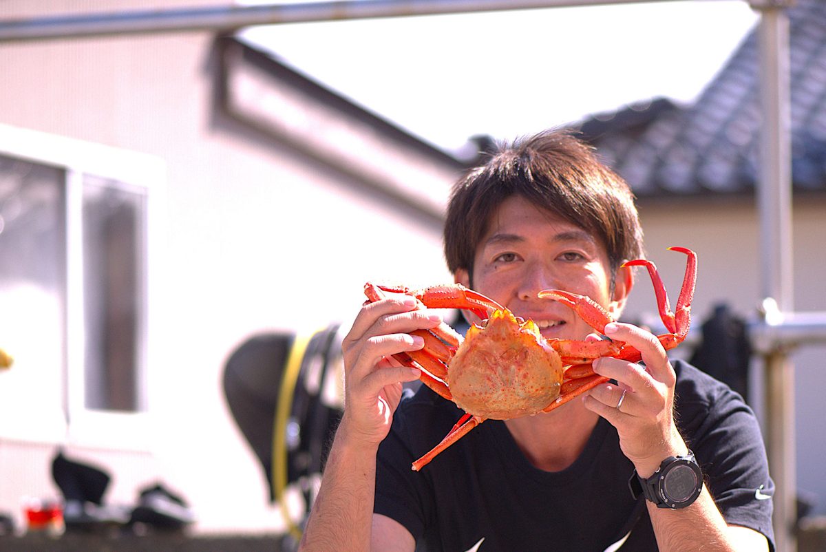 紅ズワイガニを顔の前に持つスタッフ