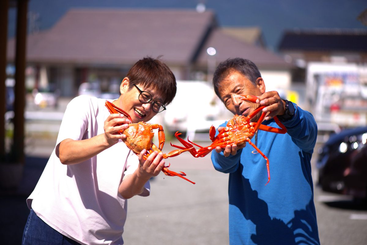 ゆでた紅ズワイガニを両手で掲げるスタッフ2人